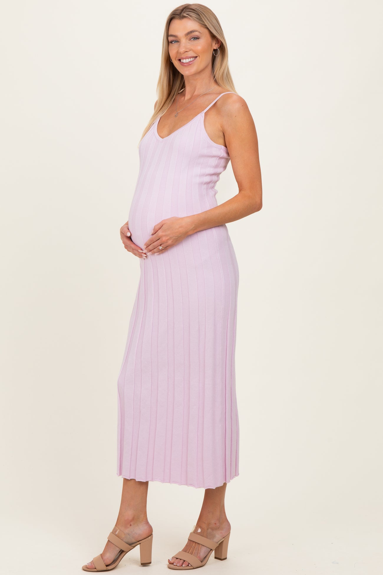 woman wearing a light pink ribbed maternity dress, showcasing her baby bump, with a fitted silhouette and midi length