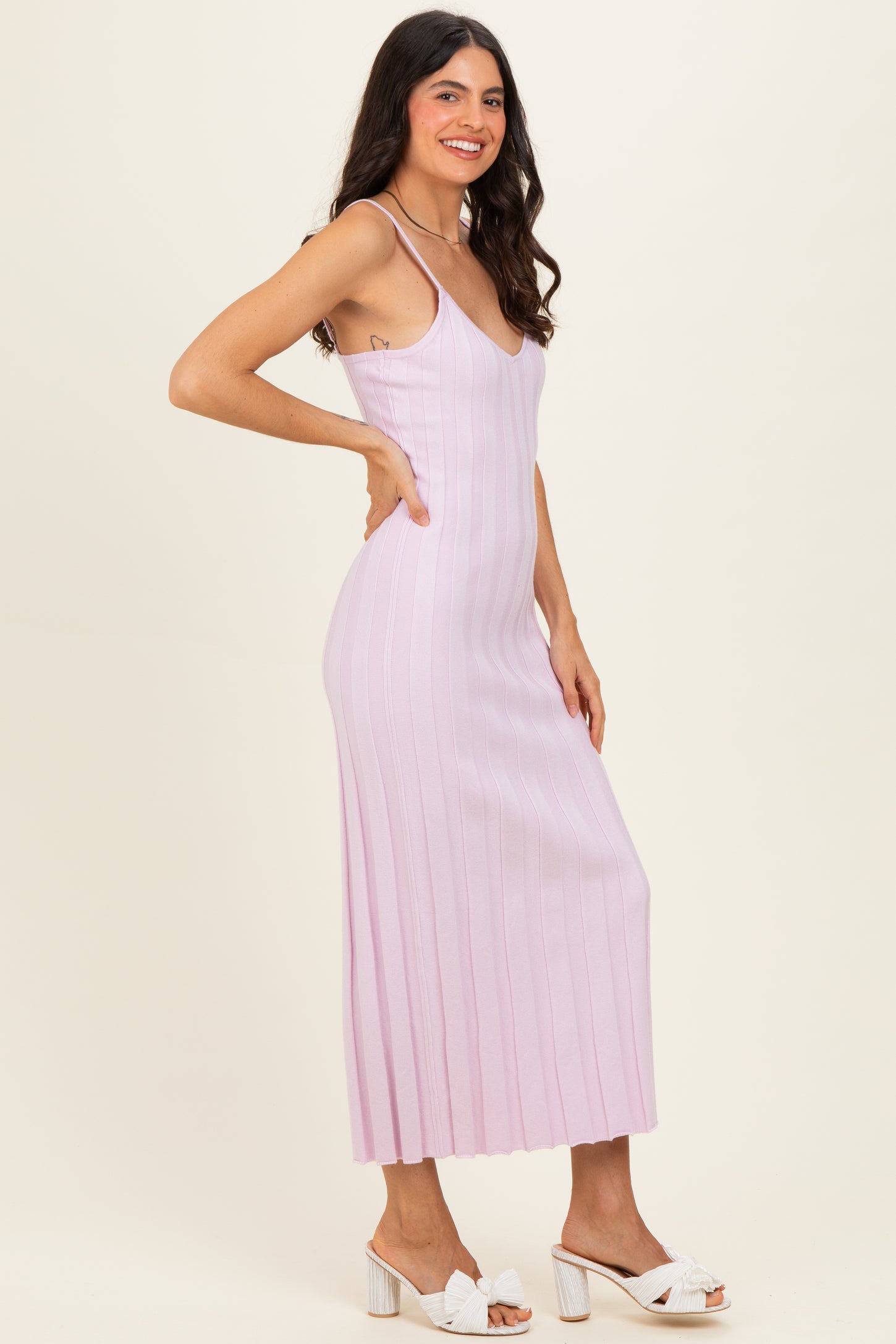 woman wearing a light pink ribbed maxi dress with thin straps and posing sideways with white heeled sandals