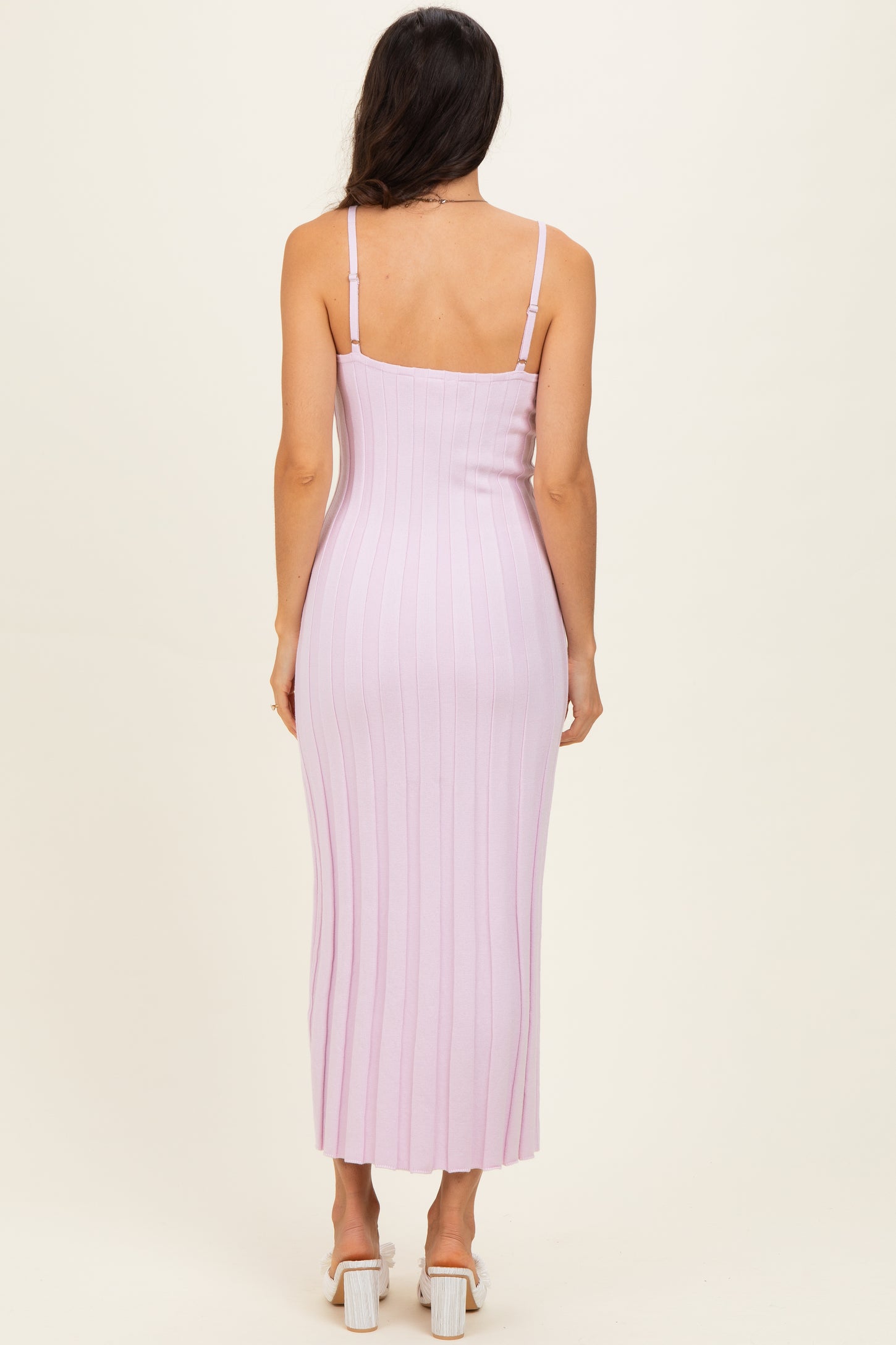 woman wearing a fitted light pink ribbed midi dress with adjustable straps seen from the back