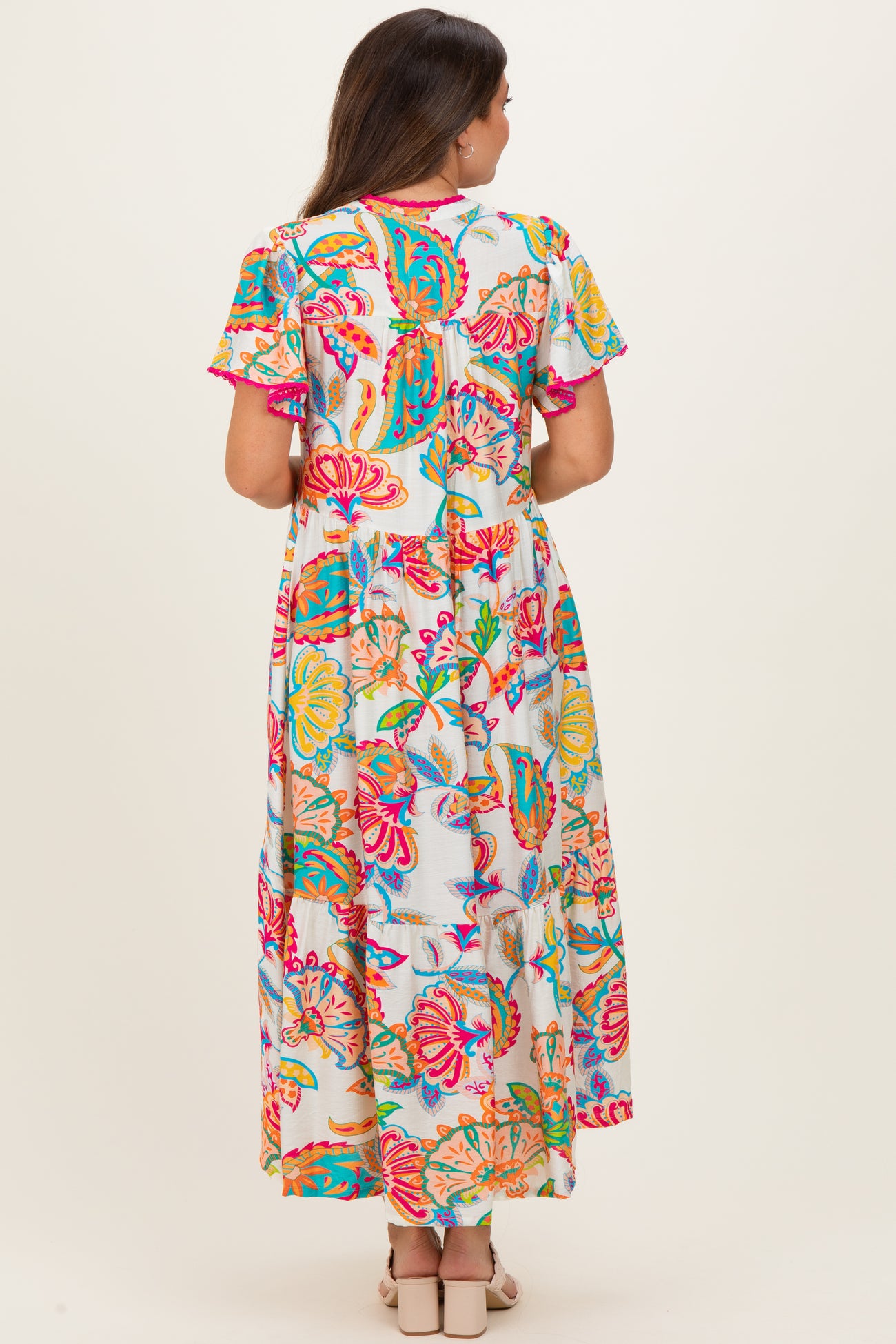 woman wearing a colorful floral maternity maxi dress, viewed from the back, with short sleeves and a flowing silhouette