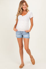 woman wearing a white maternity top with red polka dots and denim shorts, showing her baby bump