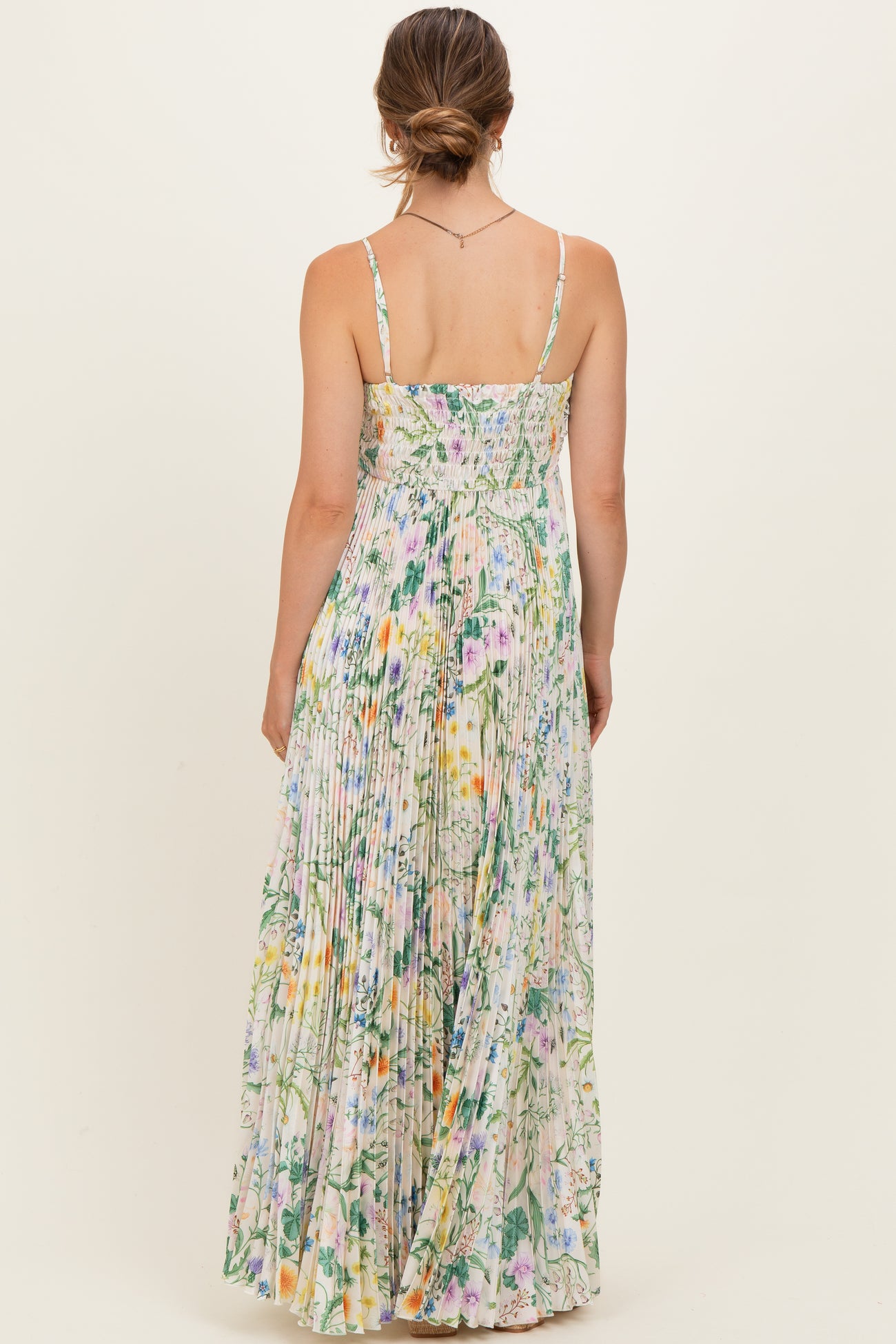 woman wearing a floral maxi maternity dress with a pleated design and adjustable straps, showing a relaxed back view