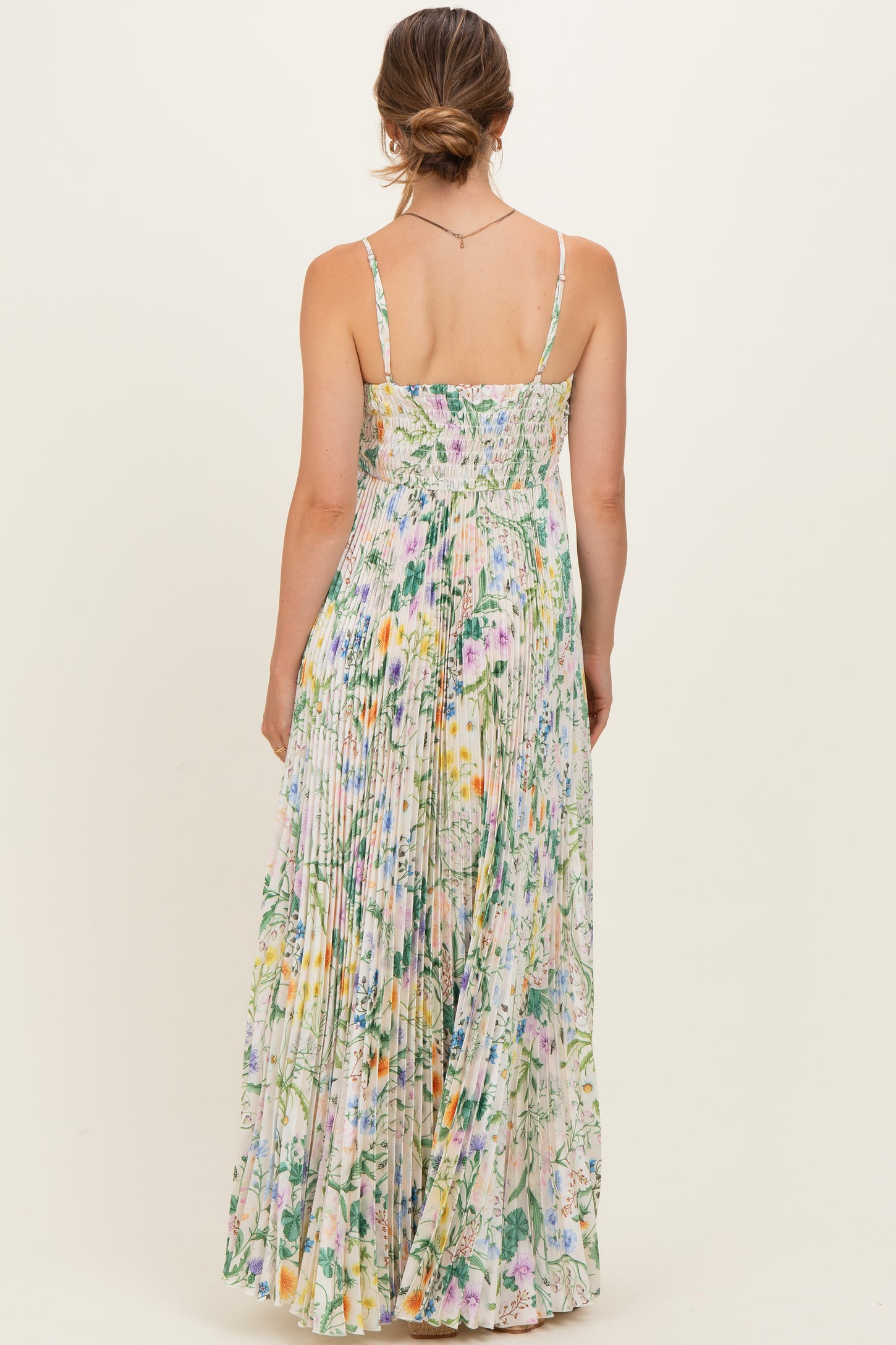 woman wearing a floral maxi maternity dress with a pleated design and adjustable straps, showing a relaxed back view