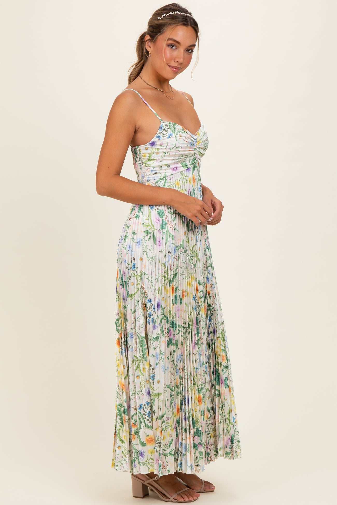 woman wearing a floral maxi dress with spaghetti straps and pleated detailing, styled with a hair accessory