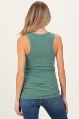 woman wearing a green ribbed maternity tank top, showing gathered side details and styled with blue jeans