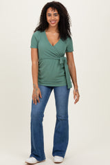 woman wearing a green short sleeve wrap top with a tie detail and flared jeans, smiling at the camera