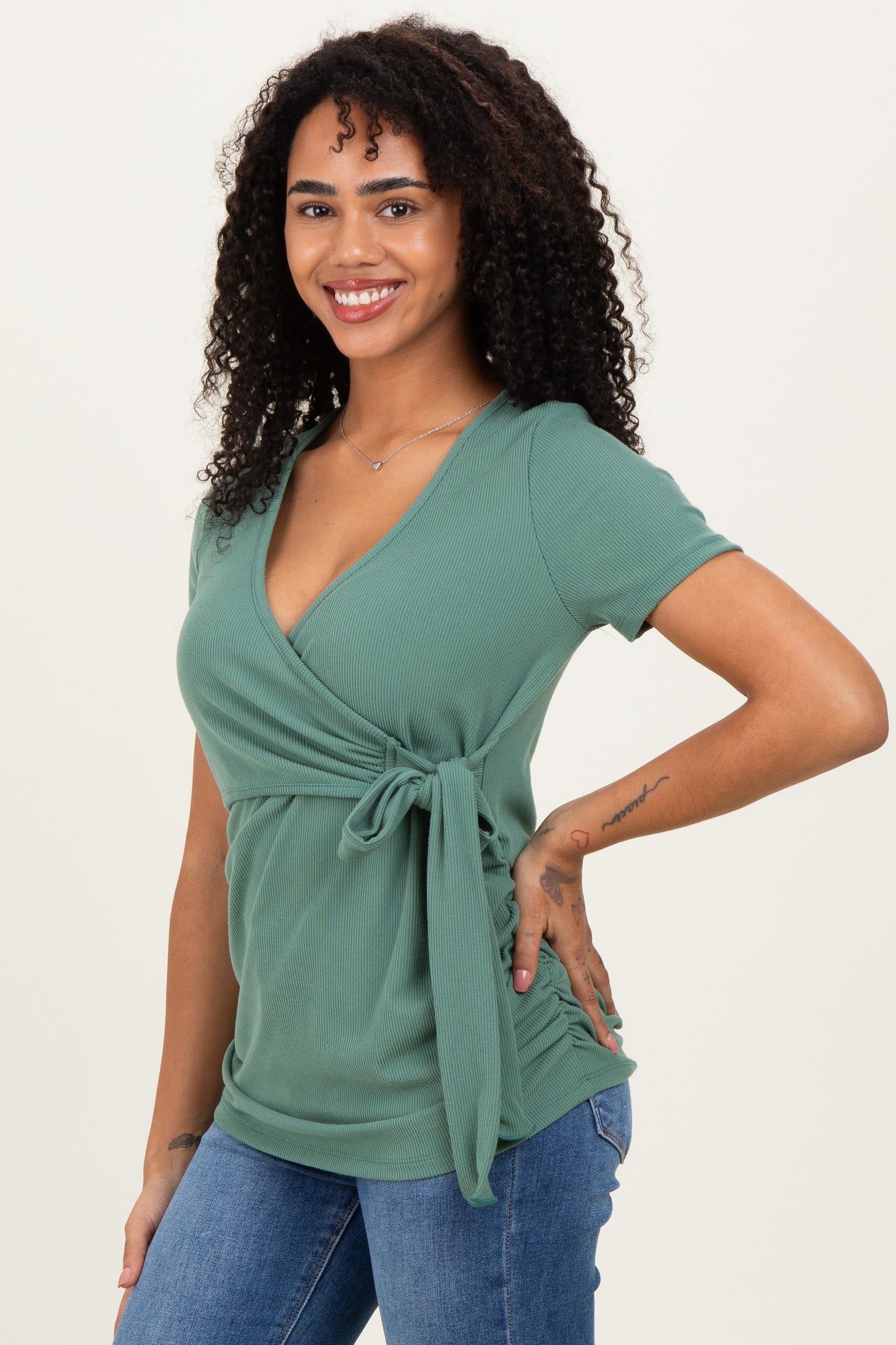 woman wearing a green short sleeve wrap top with a tie detail, paired with denim jeans