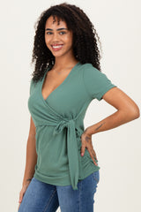 woman wearing a green short sleeve wrap top with a tie detail, paired with denim jeans
