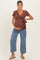 woman wearing a rust brown wrap maternity top with a tie detail and blue wide-leg maternity jeans, showing her baby bump