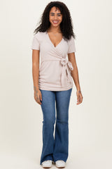 woman wearing a light pink short sleeve tie-waist top with a v-neck and flared jeans
