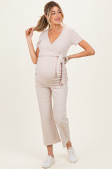 woman wearing a light beige maternity wrap top with a tie, paired with light-colored cropped pants and showing her baby bump