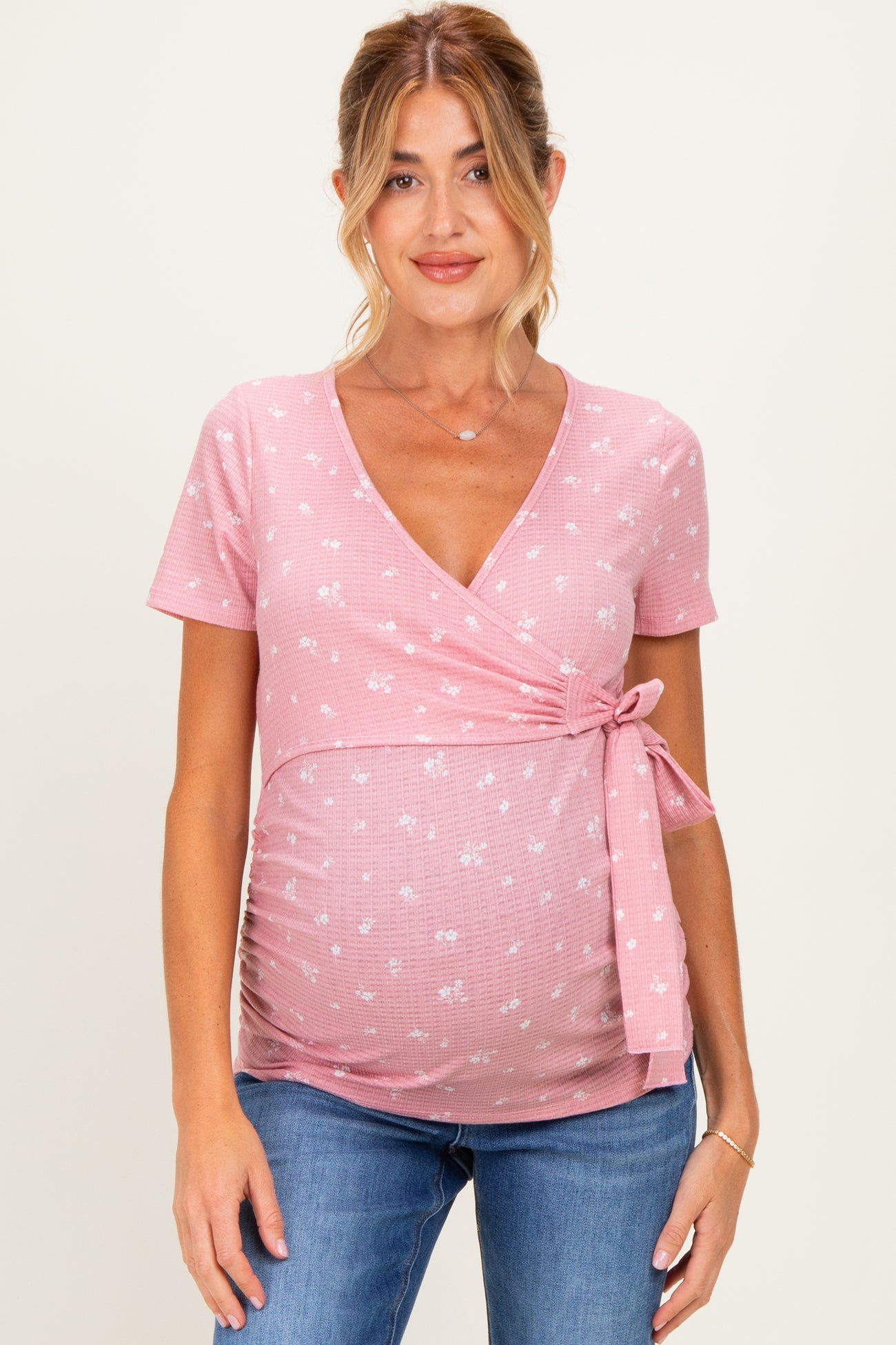 woman wearing a pink short sleeve maternity wrap top with floral print and a side tie, showcasing her baby bump