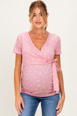 woman wearing a pink short sleeve maternity wrap top with floral print and a side tie, showcasing her baby bump