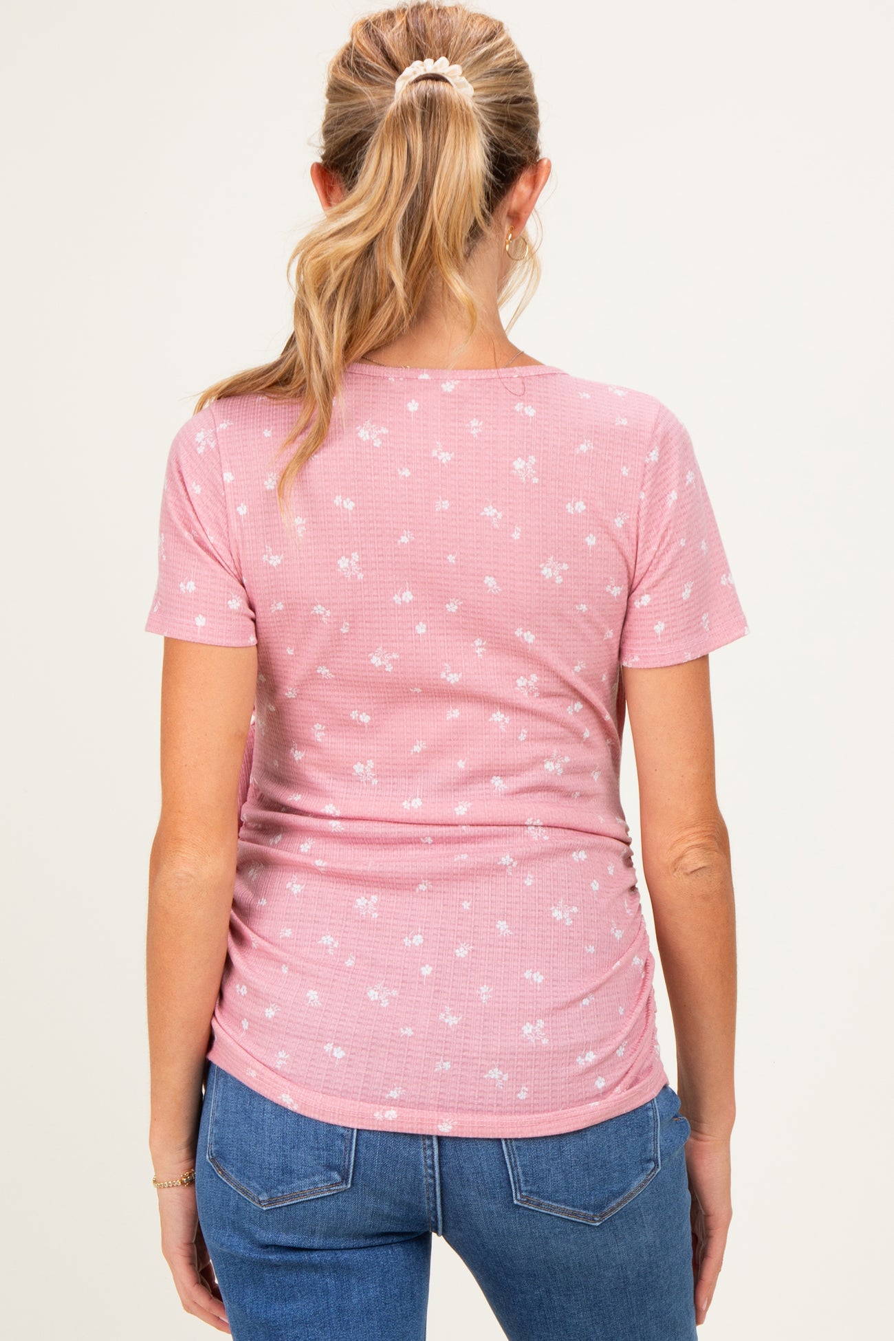 woman wearing a pink floral maternity top with a fitted style and side ruching, viewed from the back