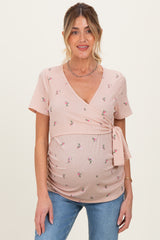 woman wearing a light pink short sleeve maternity wrap top with floral patterns and a tie at the side, showcasing her baby bump
