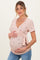 woman wearing a light pink floral print maternity top with a tie detail, holding her baby bump