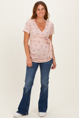 woman wearing a pink floral wrap top with short sleeves and blue bell-bottom jeans
