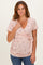 woman wearing a pink floral wrap top with short sleeves and a side tie, paired with blue jeans