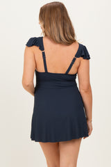 woman wearing a navy blue maternity swim dress with ruffled straps, showing a fitted bodice and flared skirt