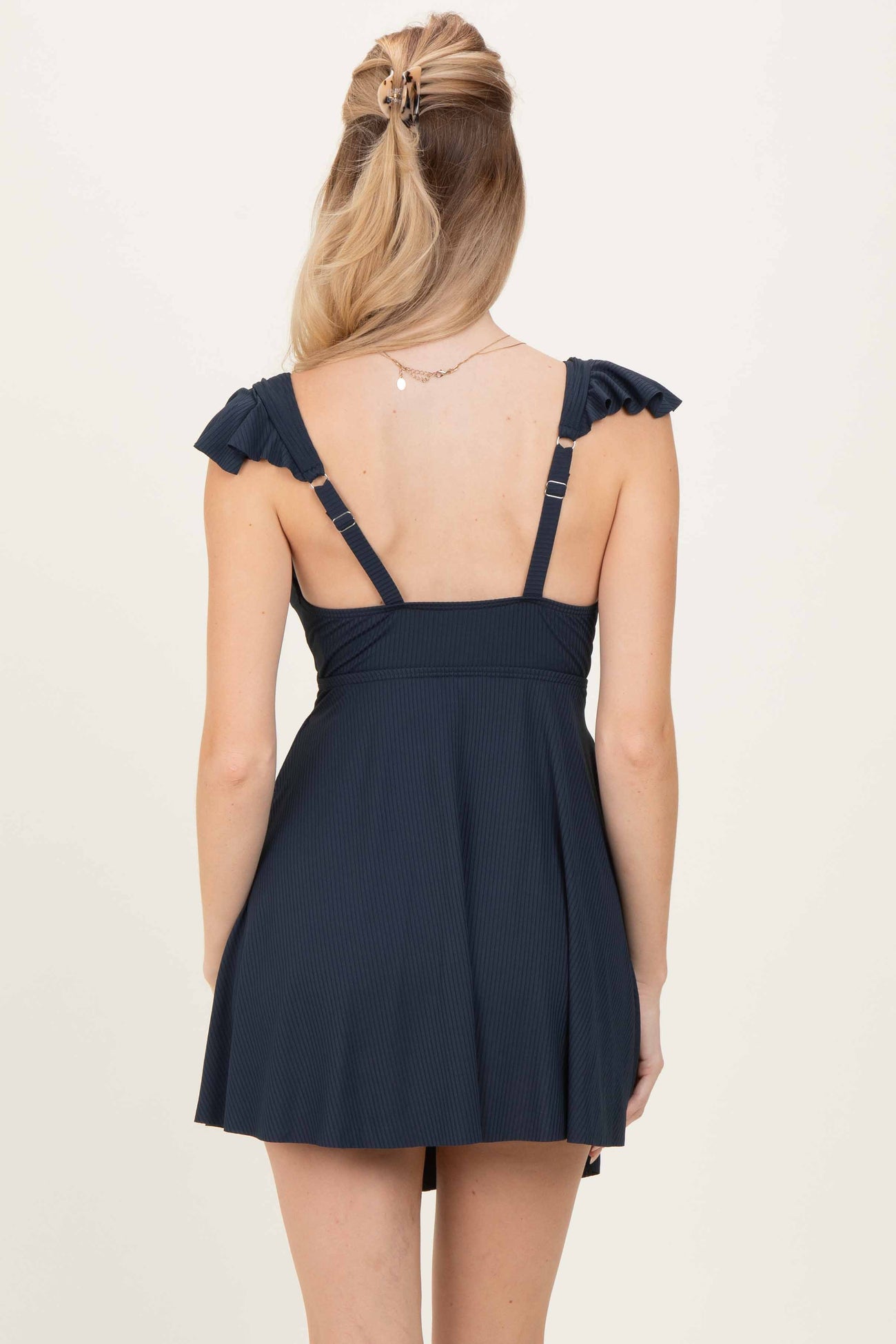 woman wearing a navy blue skater dress with ruffled straps and a fitted bodice, shown from the back