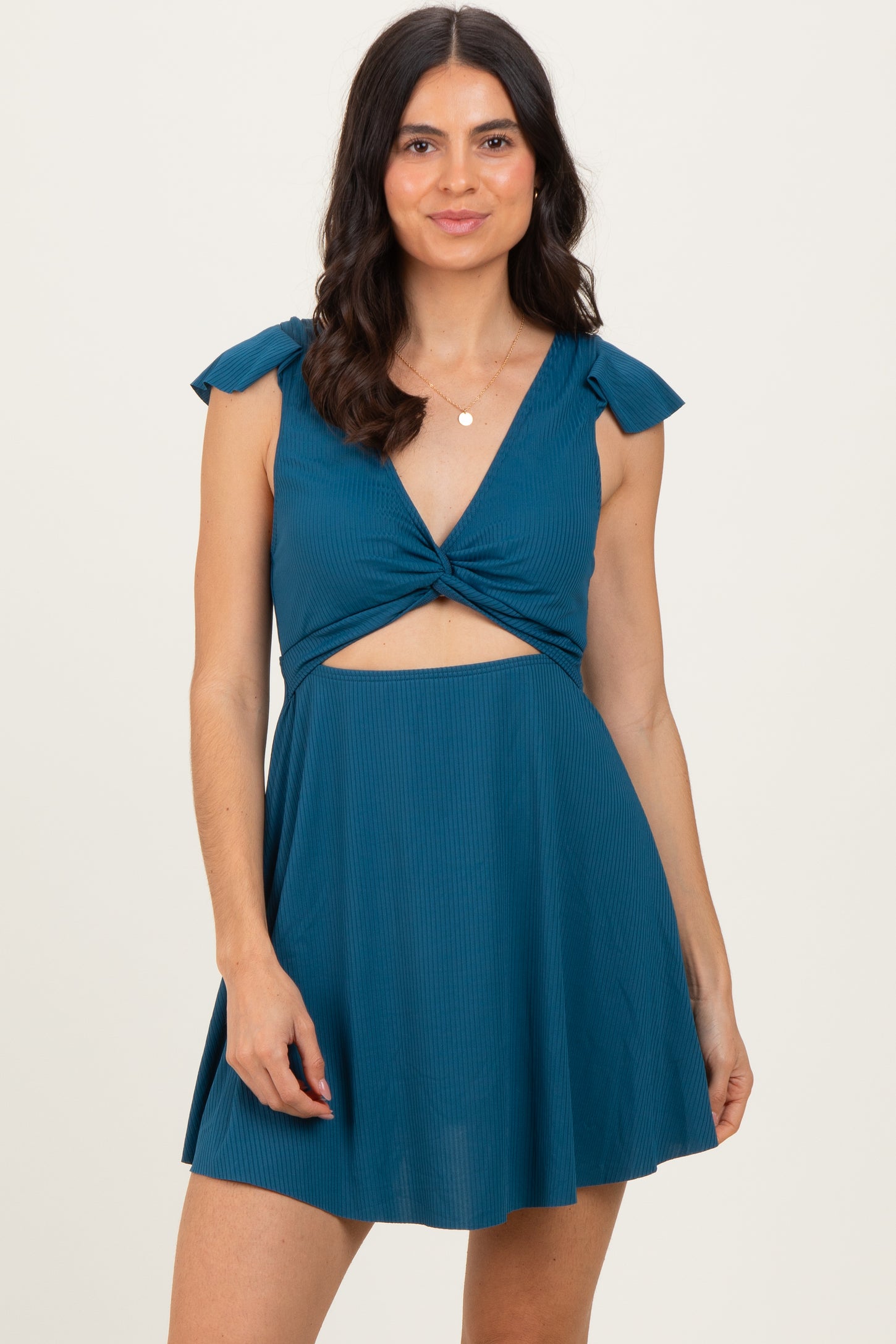 woman wearing a teal sleeveless dress with a twist front and bow details on the straps