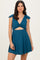 woman wearing a teal sleeveless dress with a twist front and bow details on the straps