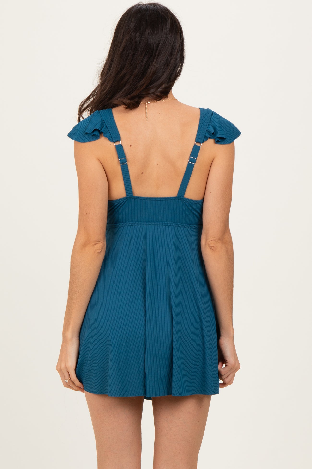woman wearing a teal sleeveless dress with ruffled straps and a fitted bodice, seen from the back