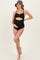 woman wearing a black maternity swimsuit with cutout detail and buttons, showing her baby bump