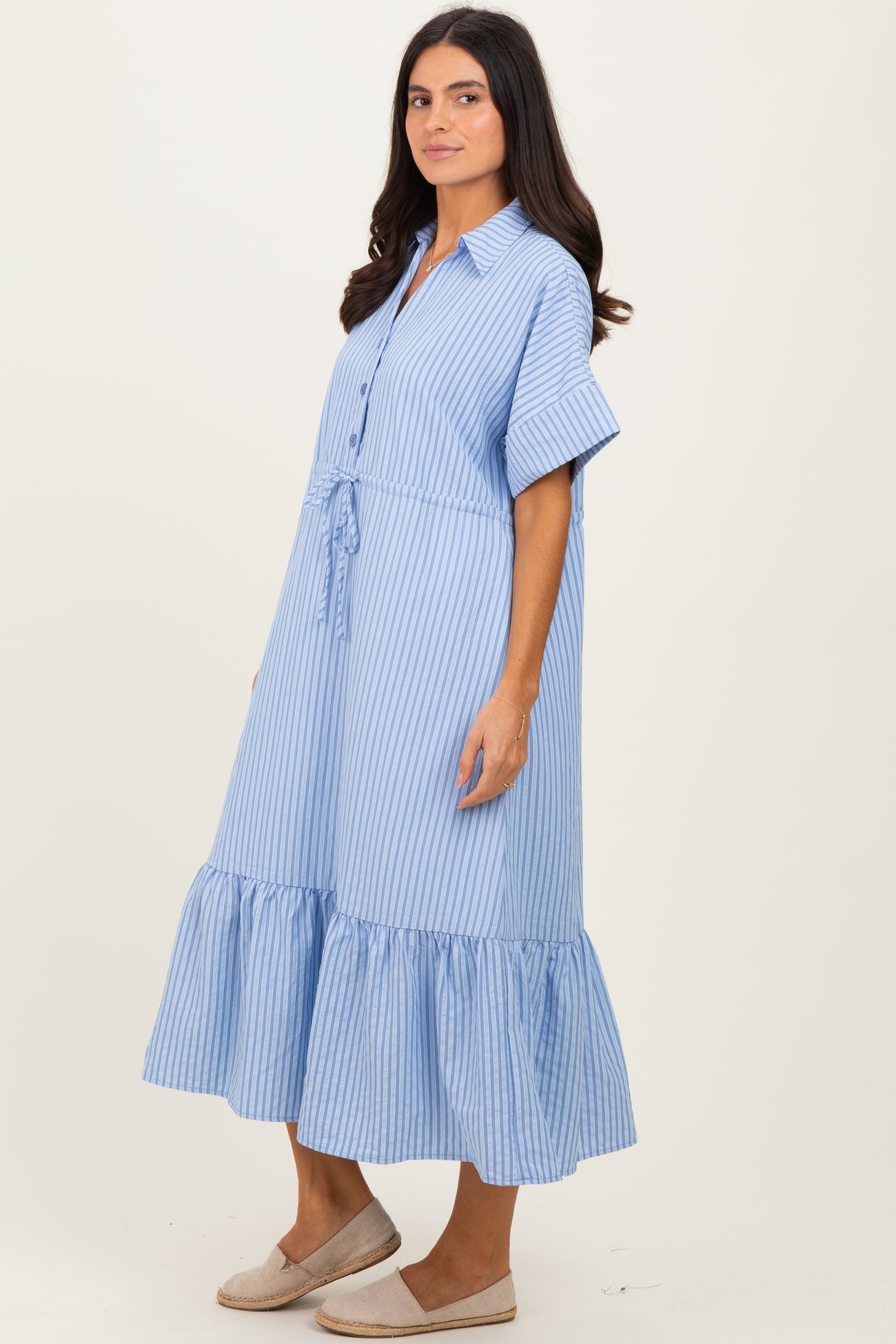 woman wearing a blue and white striped dress with short sleeves and a ruffled hem, standing sideways
