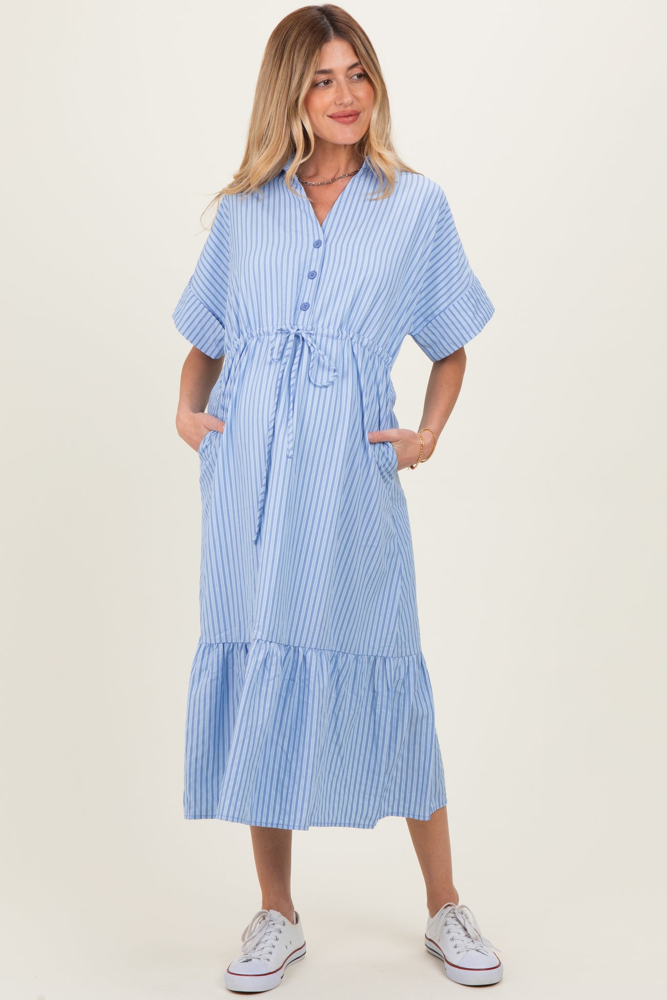 woman wearing a light blue and white striped maternity dress with tie waist and pockets, holding her baby bump