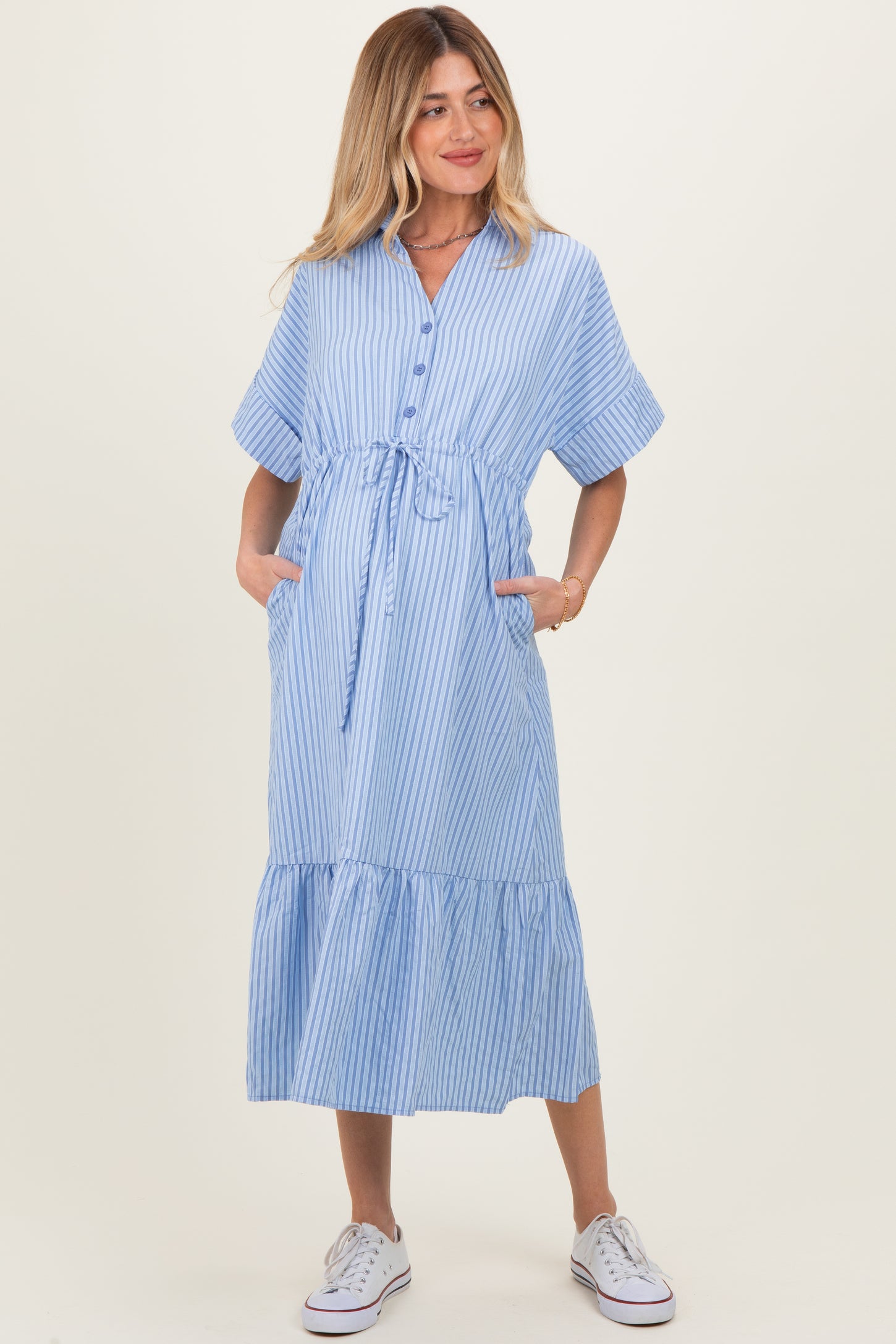 woman wearing a light blue and white striped maternity dress with tie waist and pockets, holding her baby bump