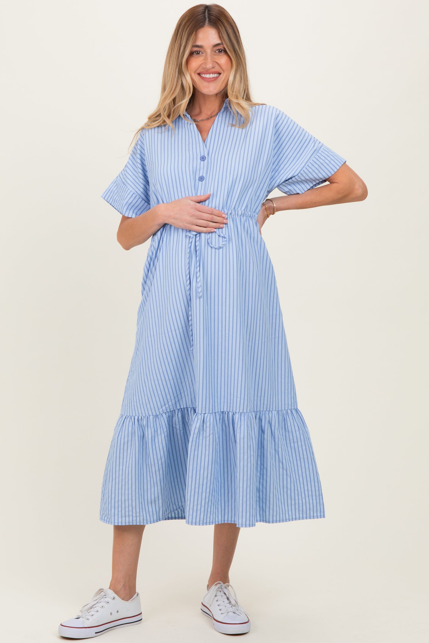 woman wearing a light blue striped maternity dress with short sleeves and a tiered ruffle hem, holding her baby bump