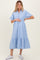 woman wearing a light blue striped maternity dress with short sleeves and a tiered ruffle hem, holding her baby bump