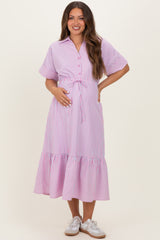 woman wearing a pink and white striped maternity dress with a tie waist and ruffled hem, gently cradling her baby bump