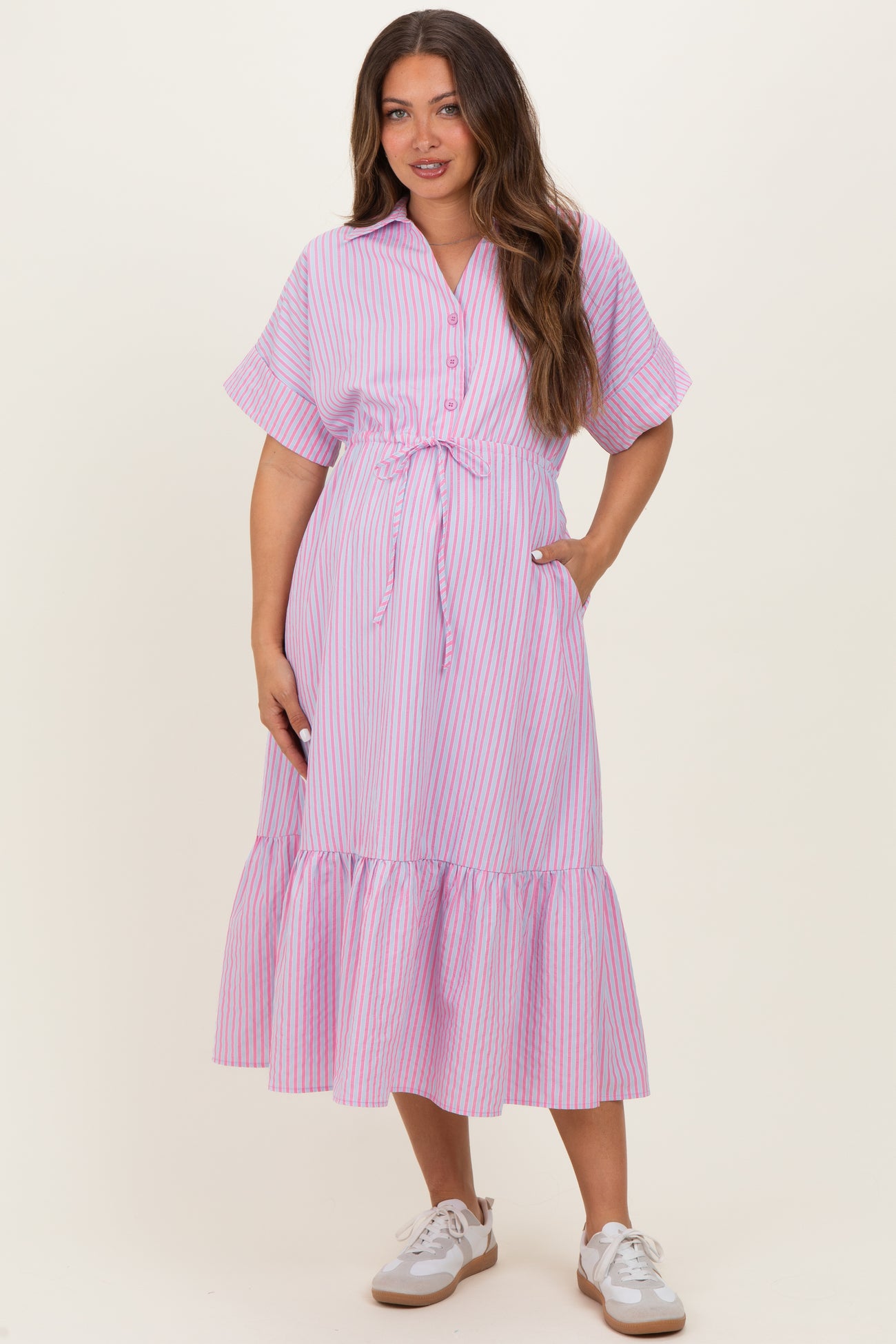 woman wearing a pink and white striped maternity dress with short sleeves and a tiered hem, holding her baby bump