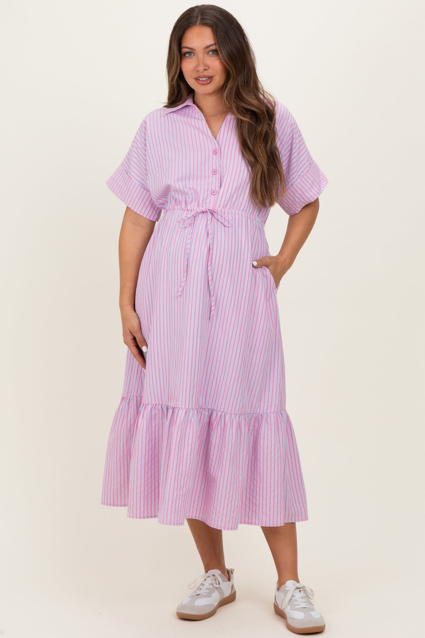 woman wearing a pink and white striped maternity dress with short sleeves and a tiered hem, holding her baby bump