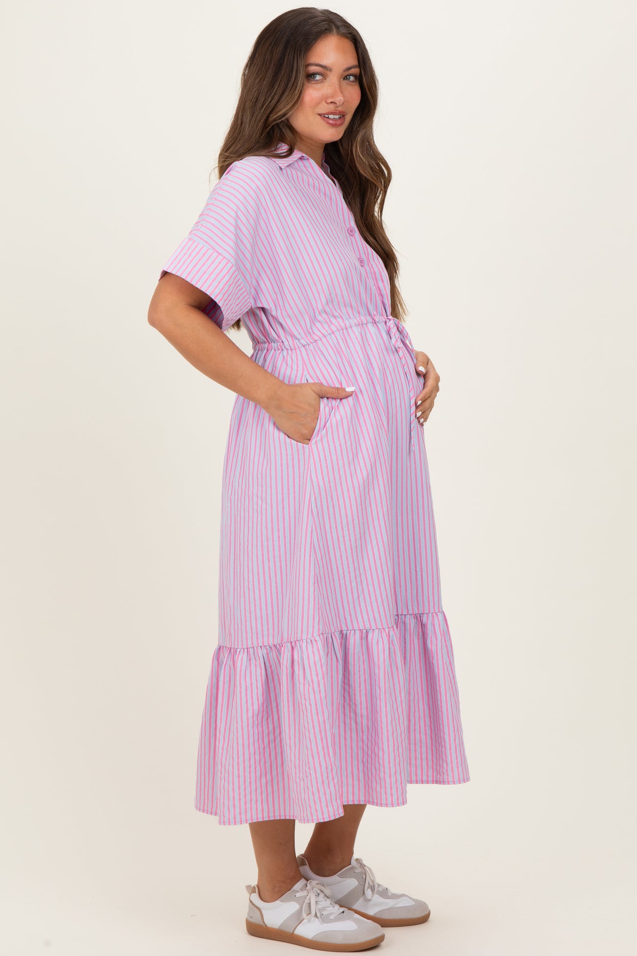 woman wearing a pink and white striped maternity dress with a ruffled hem and pockets, holding her baby bump
