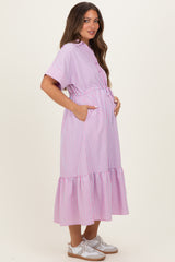 woman wearing a pink and white striped maternity dress with a ruffled hem and pockets, holding her baby bump