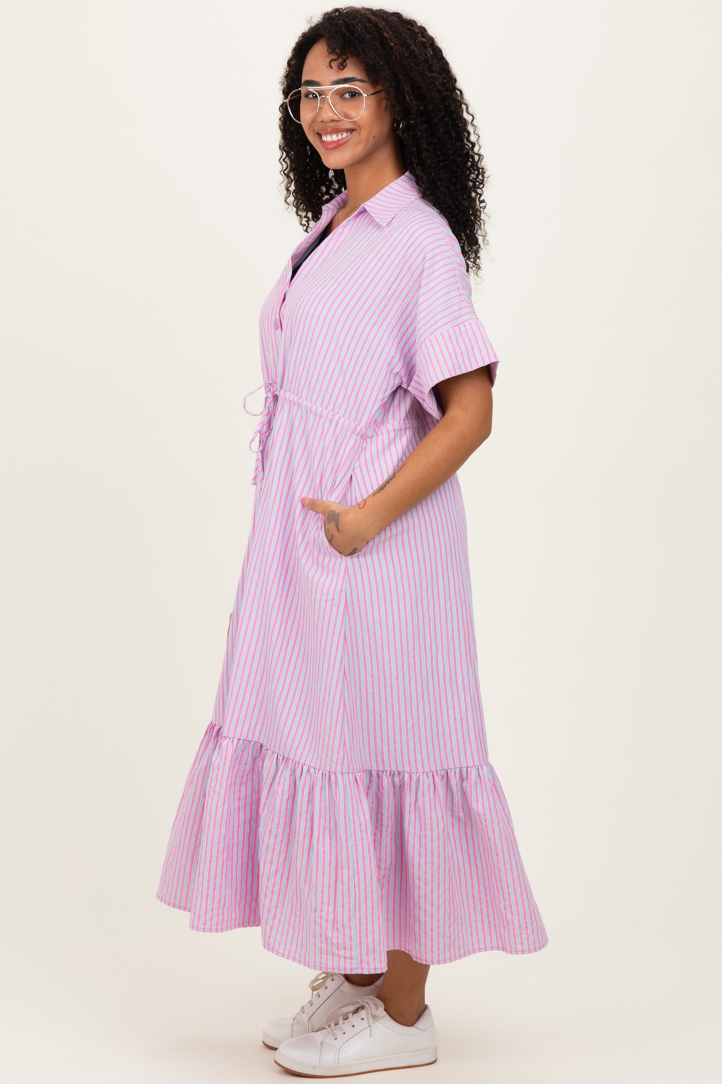 woman wearing a pink and purple striped midi dress with short sleeves and a ruffled hem, standing sideways and smiling