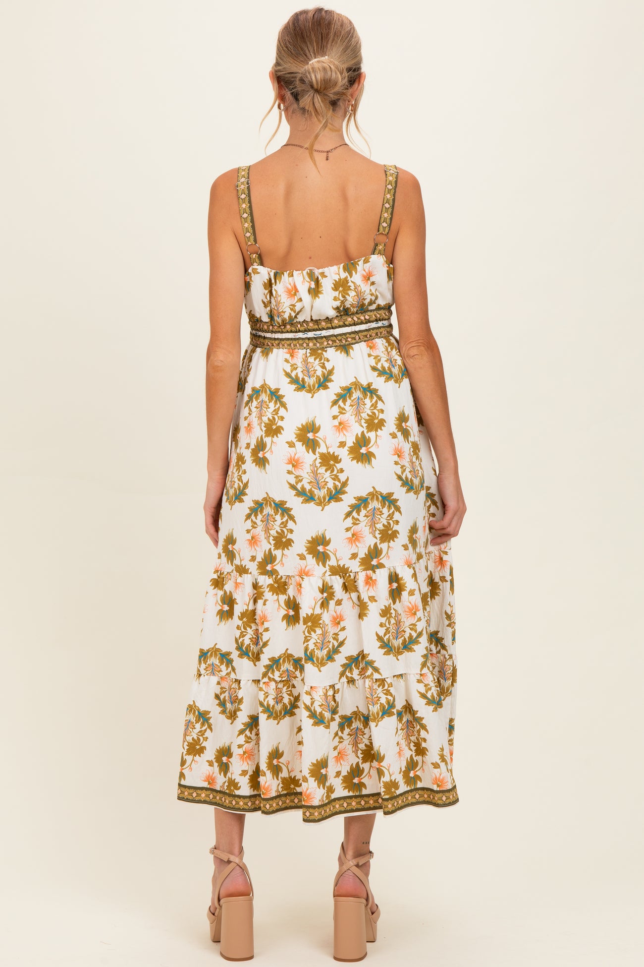 woman wearing a white floral maternity maxi dress with a green belt and adjustable straps, showing a baby bump
