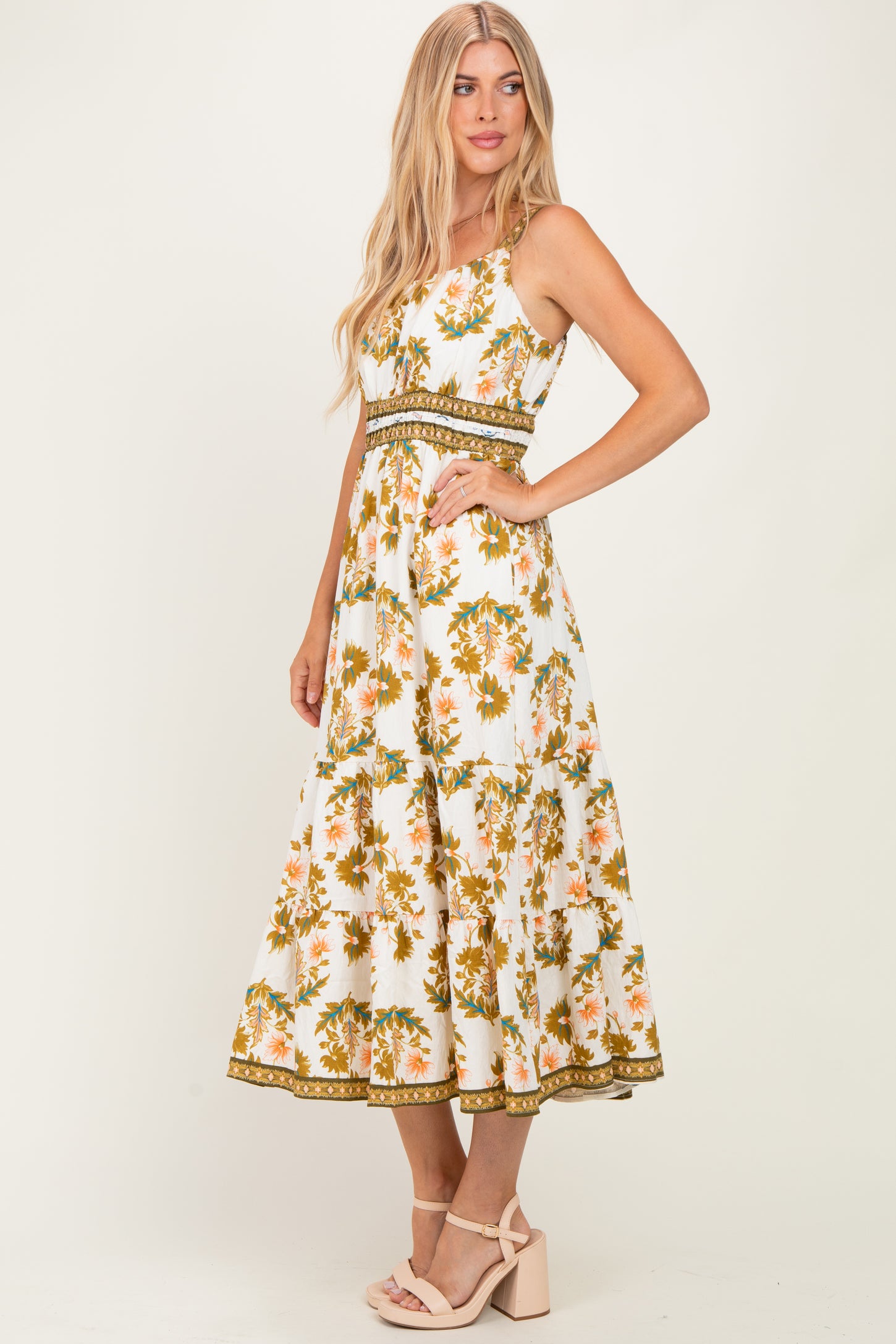 woman wearing a white floral maxi dress with orange and green details, styled with a fitted waist and flared skirt