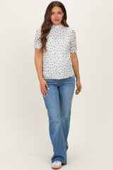 woman wearing a white maternity top with floral print and short sleeves, paired with light blue flared jeans, showing her baby bump