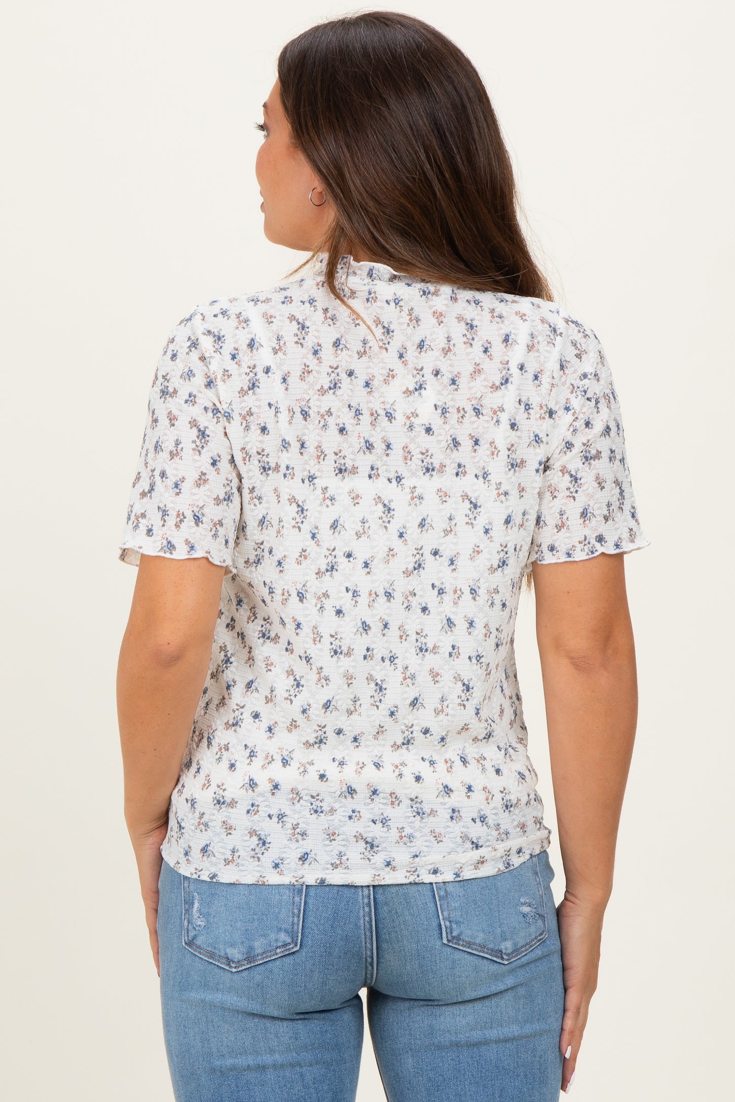 woman wearing a sheer white floral maternity top with short sleeves and relaxed fit, showing her back
