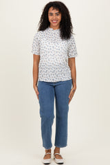 woman wearing a white short sleeve floral print top and blue high-waisted jeans standing against a neutral background