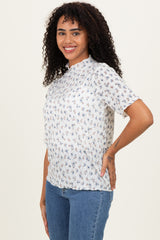 woman wearing a white short sleeve floral blouse and blue jeans, smiling at the camera