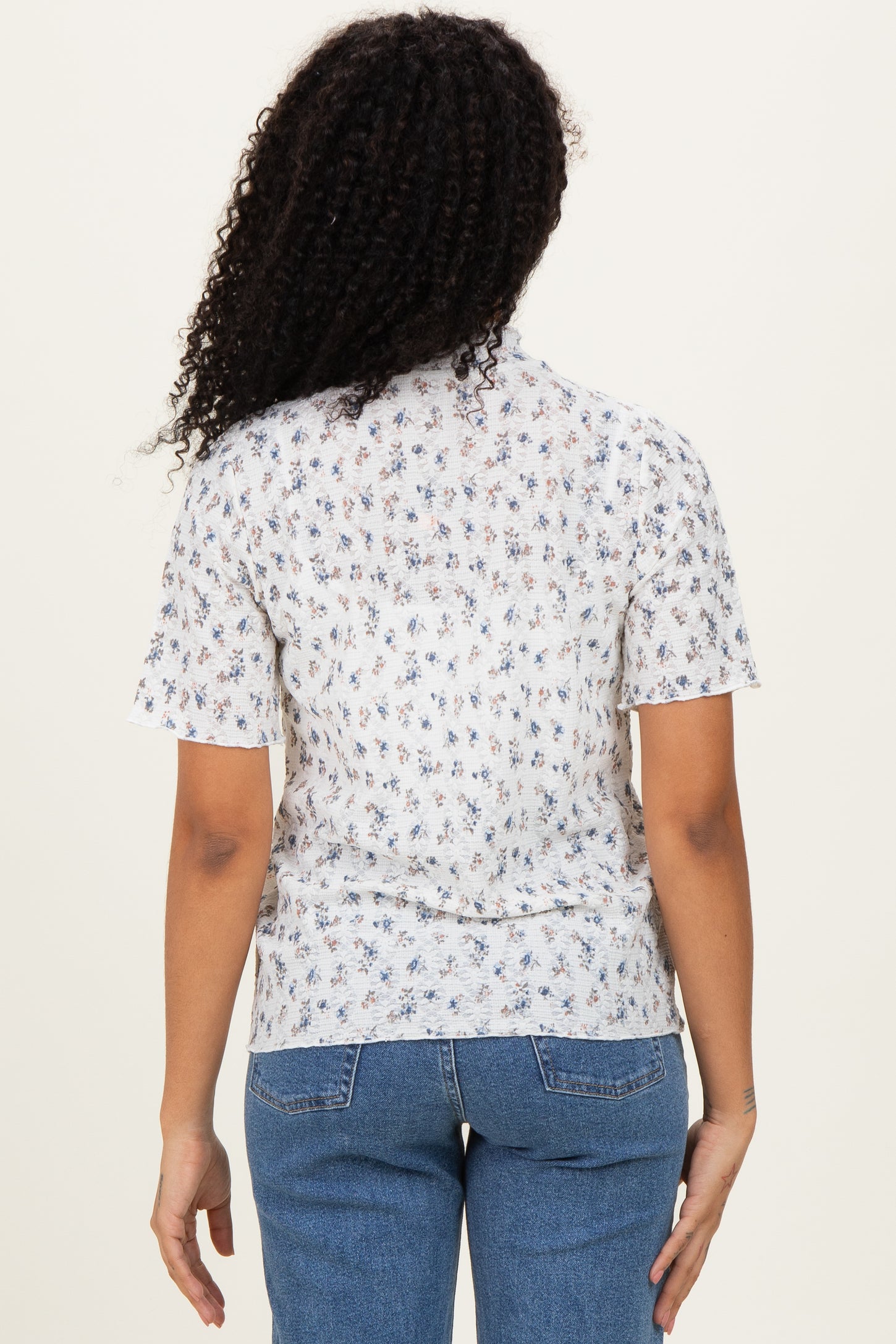 woman wearing a white short sleeve top with a floral pattern and light blue jeans, seen from the back