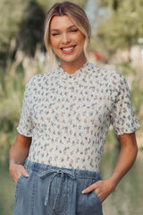 woman wearing a cream short sleeve maternity top with floral pattern and scalloped neckline, smiling outdoors