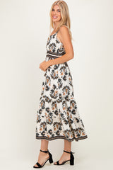 woman wearing a white floral maxi dress with spaghetti straps and detailed waistband, standing and smiling