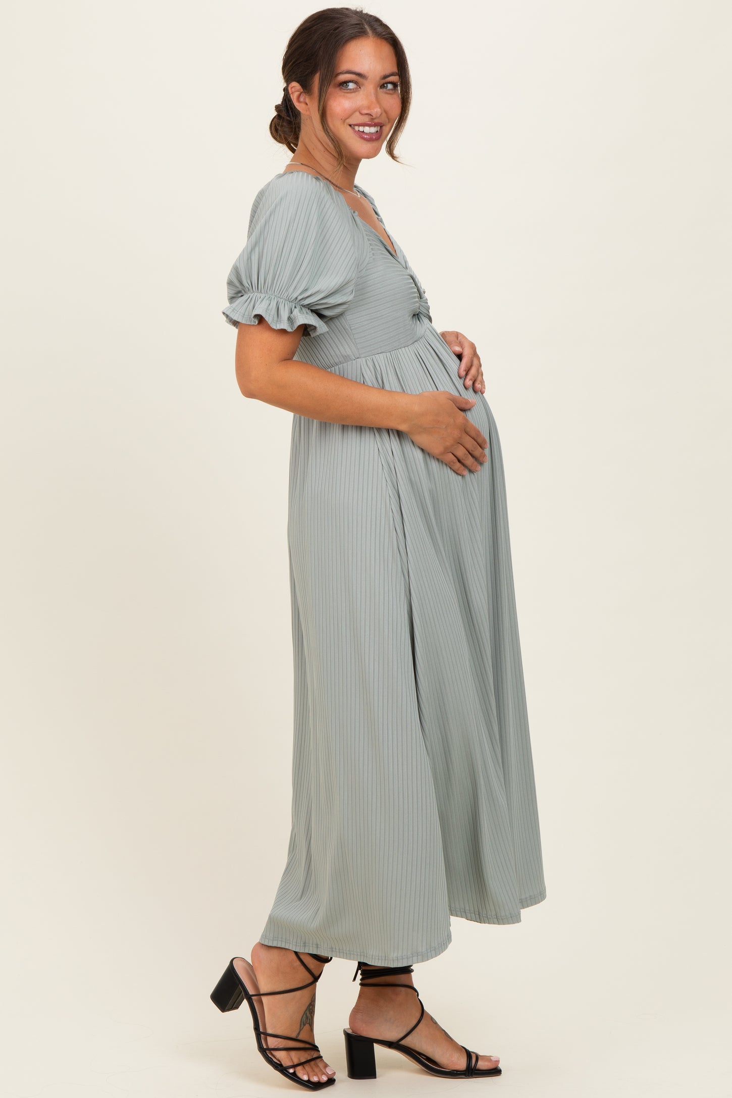 woman wearing a sage green ribbed maternity dress with a cinched waist and puff sleeves, showing her baby bump
