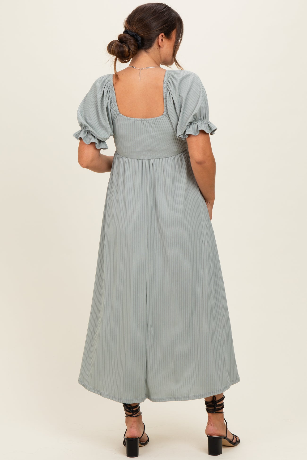 woman wearing a sage green pleated maternity dress with puff sleeves and a square back view.